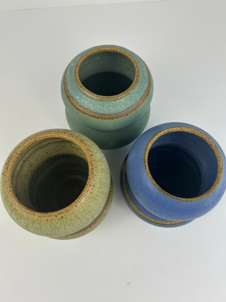 Three handmade ceramic vases with a rustic stoneware finish, displayed on a clean white background. The planters feature three distinct glazes: a textured light green, a deep cobalt blue, and a speckled beige.