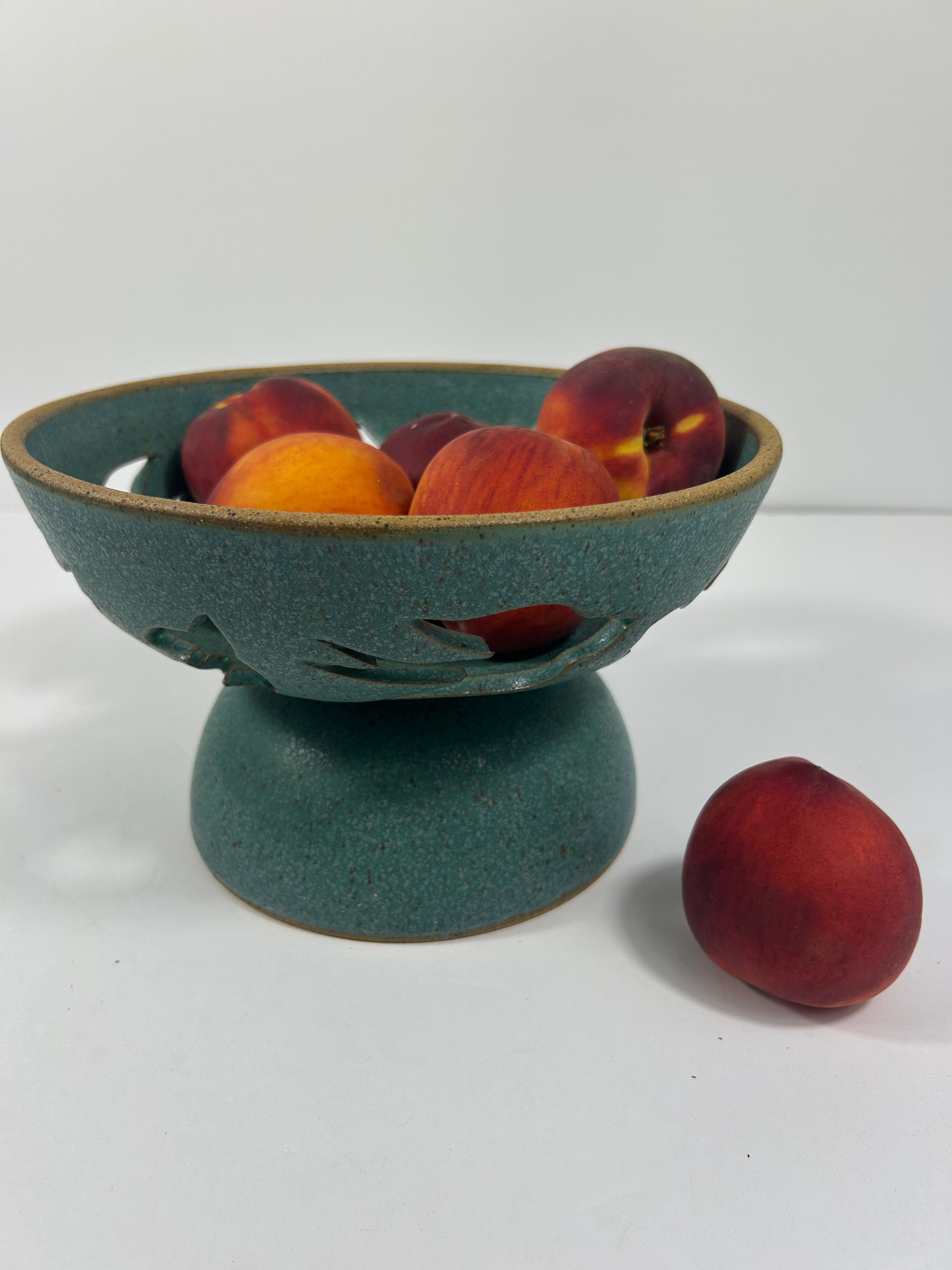 Stoneware teal pedestal bowl with swallow cut-outs with peaches