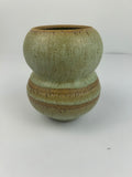 A handmade ceramic vase with a distinctive double-bulb shape, featuring a textured sage green glaze with earthy brown and gold-toned accents, set against a plain light gray background.