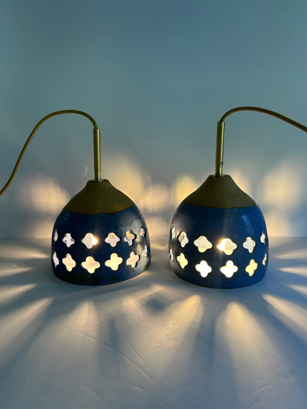 2 Cobalt blue ceramic pendant lamp on speckled clay with gold cord and moroccan piercings casting shadows