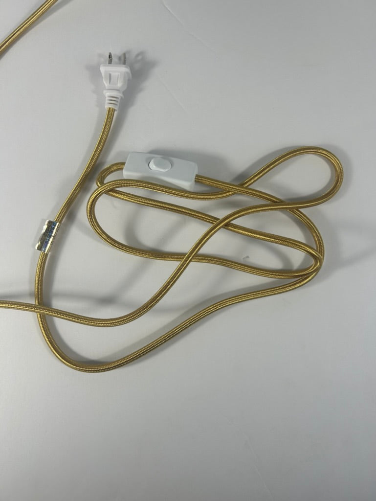 A gold-colored fabric-covered cord with a white plastic plug and a white inline switch, shown on a plain light gray background.