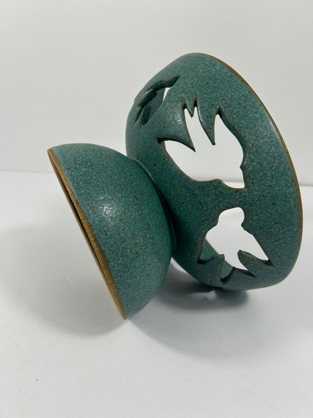 Stoneware teal pedestal bowl with swallow cut-outs tipped on side