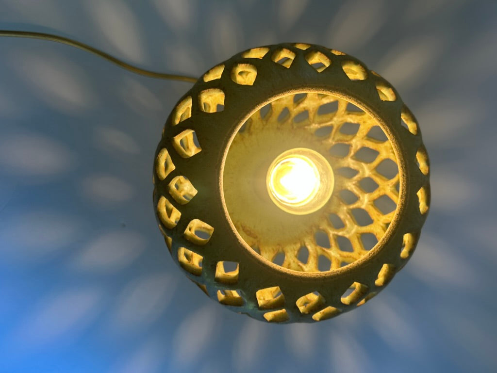 A glowing decorative pendant lamp with a circular cutout shade casting star-like shadows on a blue background.