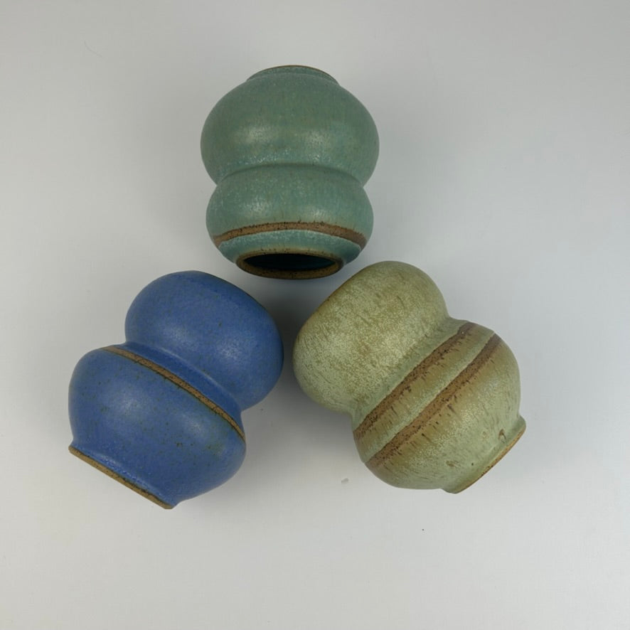 Three small ceramic gourd-shaped vases with rounded bodies and flared rims, shown on a plain light background. One vase is aqua green, one is medium blue, and one is pale sage green with a brown glazed band.