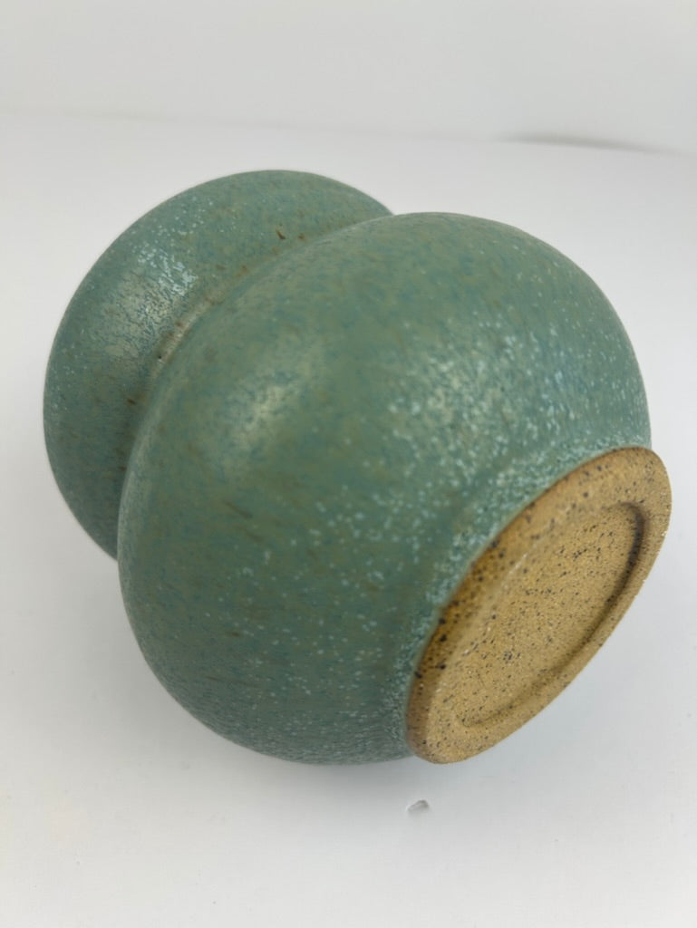 A handmade ceramic vase with a textured, speckled teal-green glaze and a natural tan clay base, photographed on a plain white background.