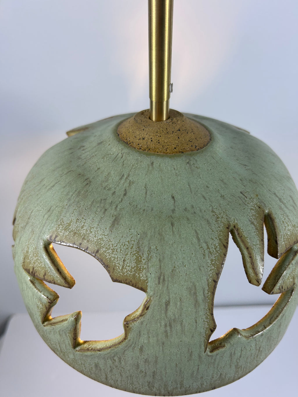 Close-up of Stoneware green speckled pendant lamp with bird piercings and gold cord 