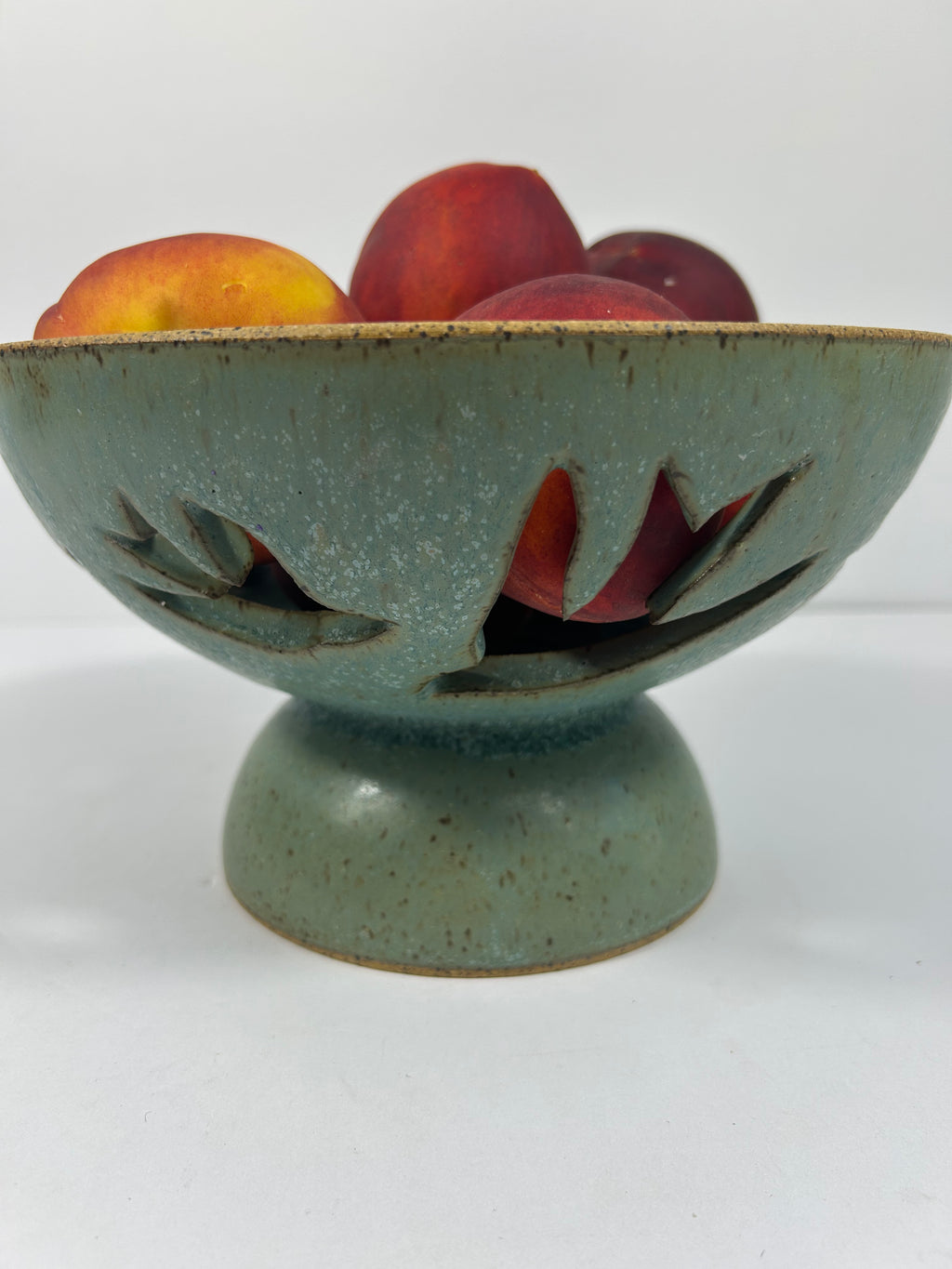Stoneware green-blue pedestal bowl with bird piercings holding peaches