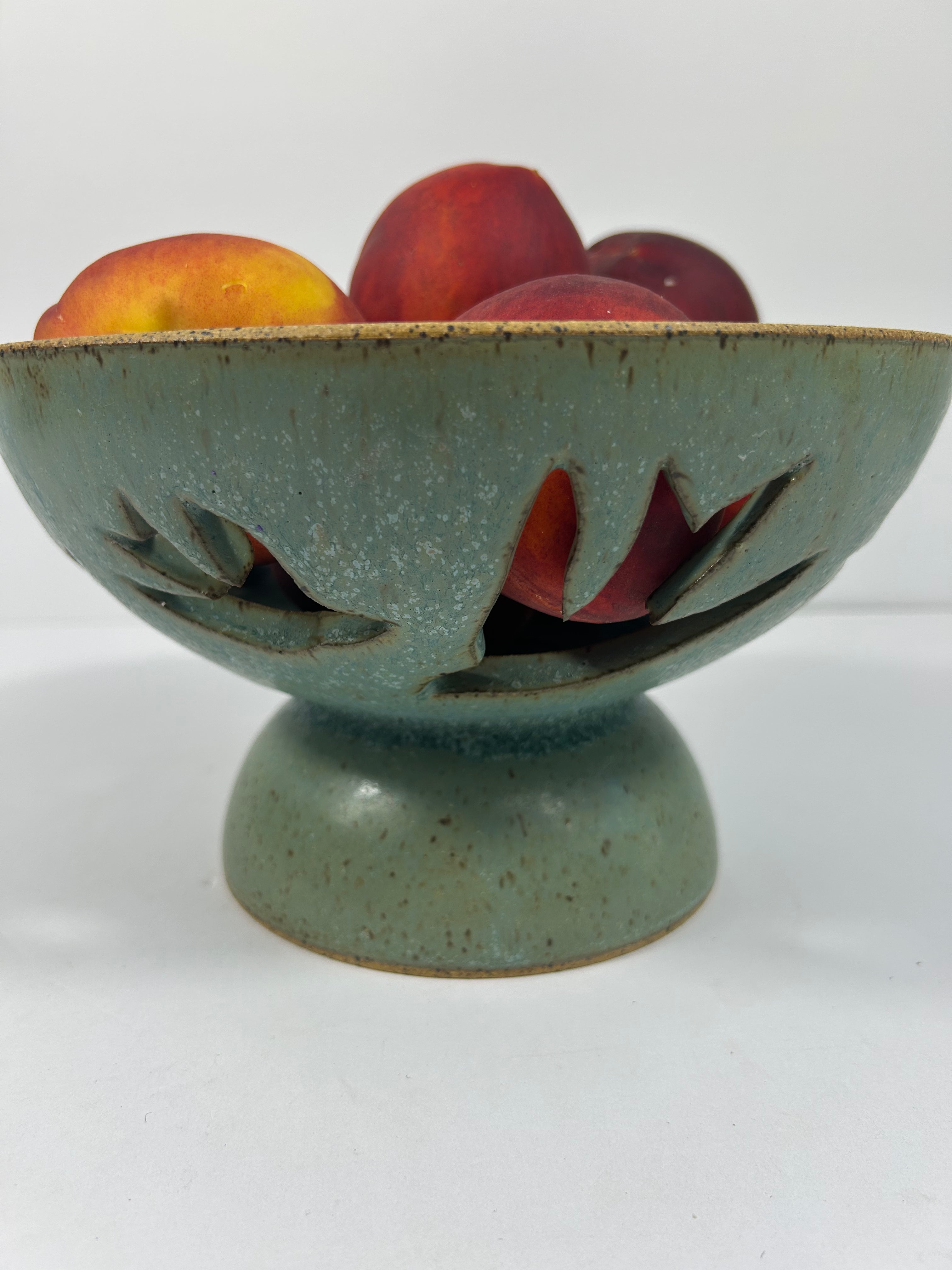 Stoneware green-blue pedestal bowl with bird piercings holding peaches