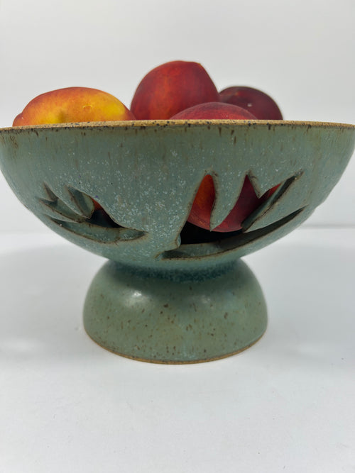 Stoneware green-blue pedestal bowl with bird piercings holding peaches