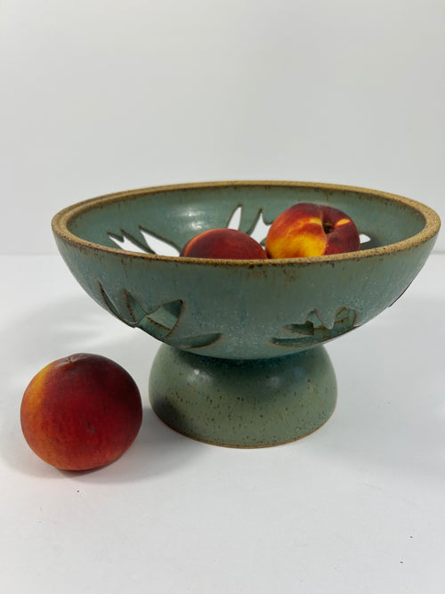 Stoneware green-blue pedestal bowl with bird piercings holding peaches