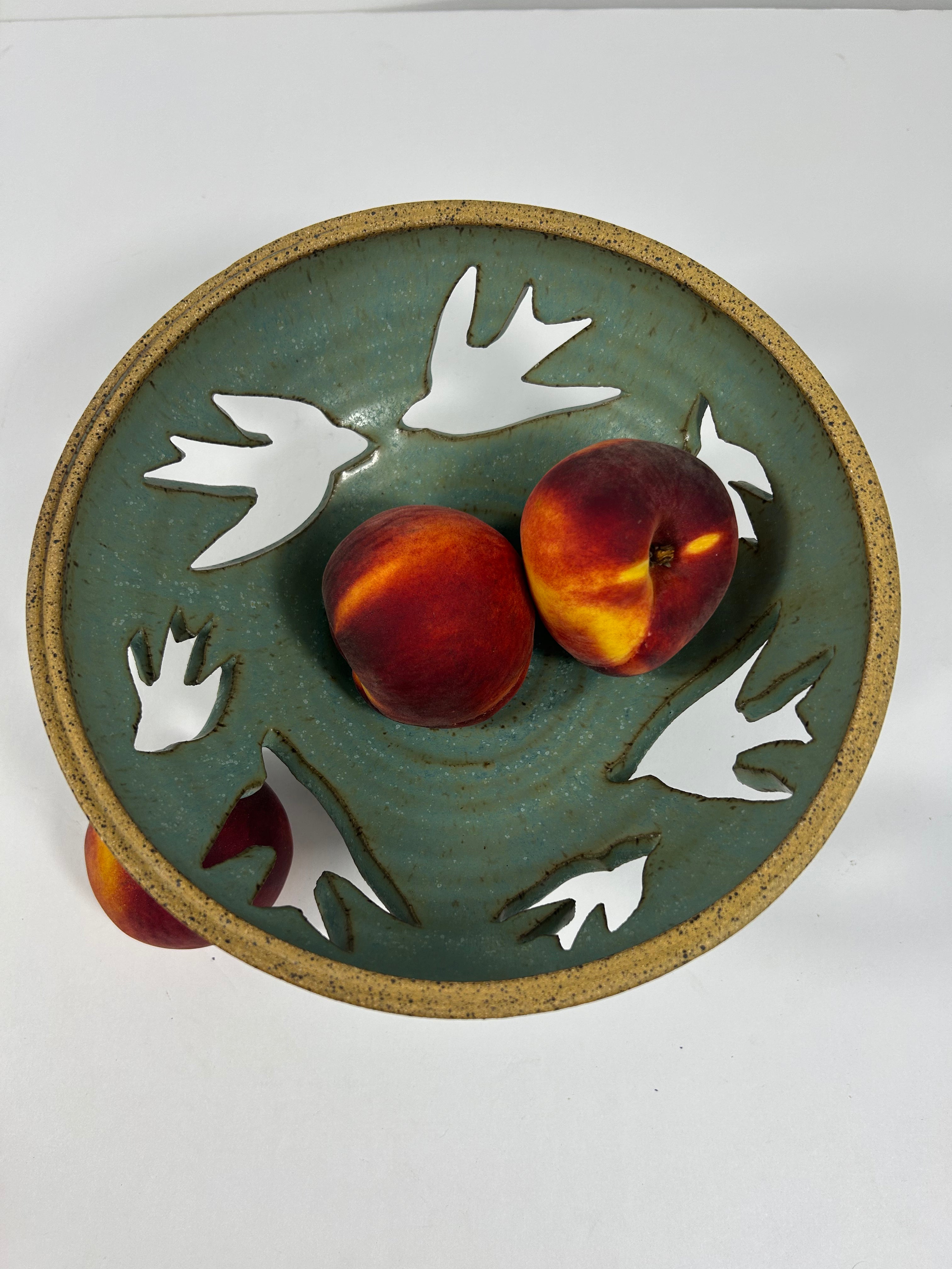 Stoneware green-blue bowl with bird piercings holding peaches